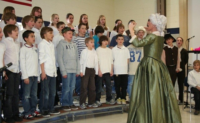 Angie in a period costume conducting choir students during a school residency.